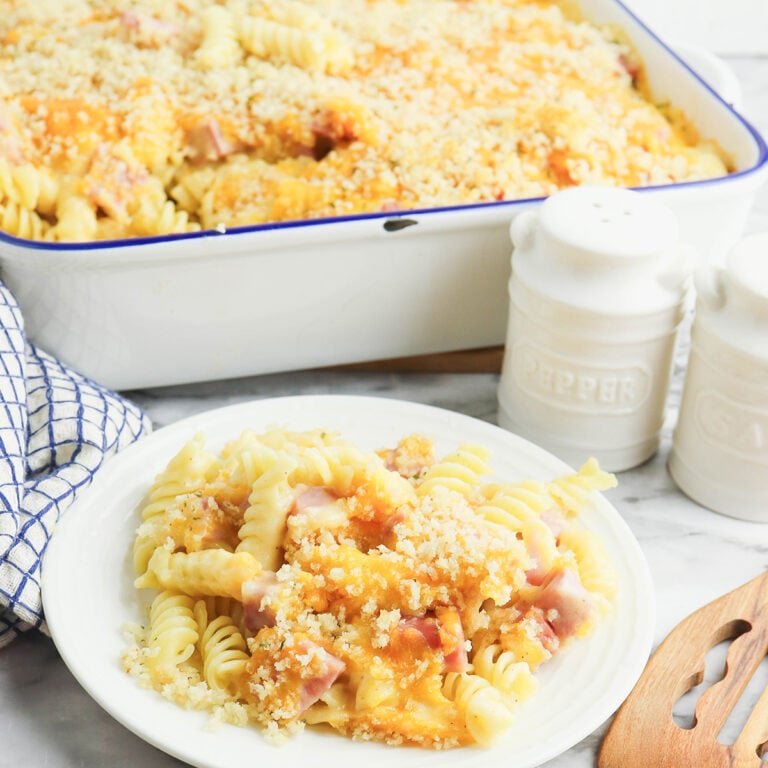 A serving of Ham and Cheese Casserole on white plate with baked casserole dish in behind it.