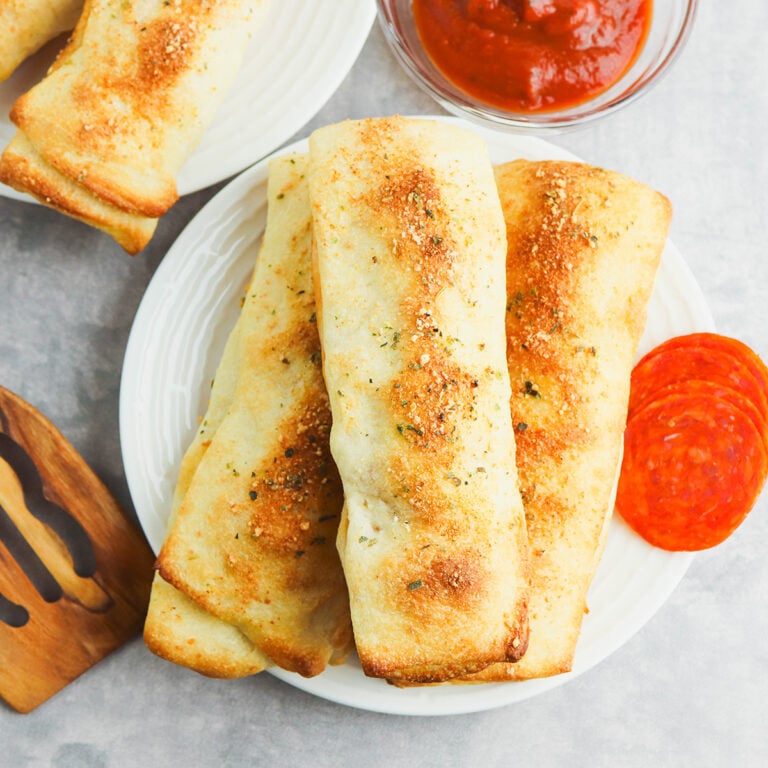 Three Pepperoni Breadsticks stacked on white plate.