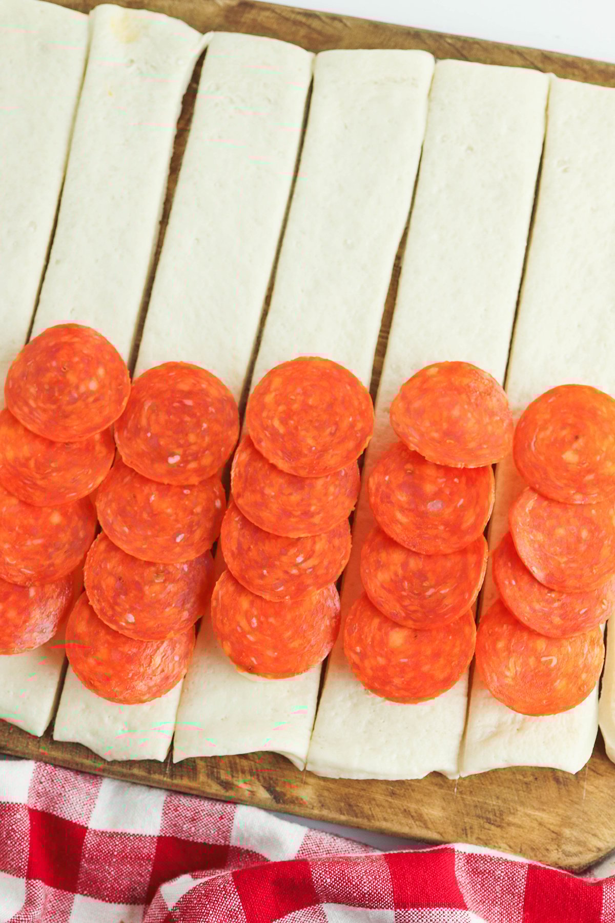 Pepperoni added on top of cheese sticks on pizza dough strips.