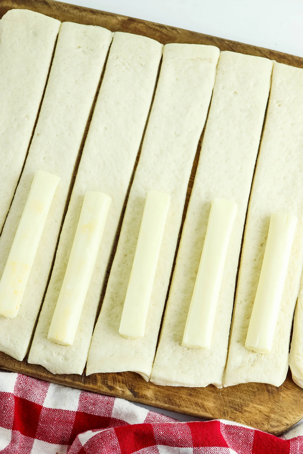 String cheese placed on pizza dough strips on wooden board.