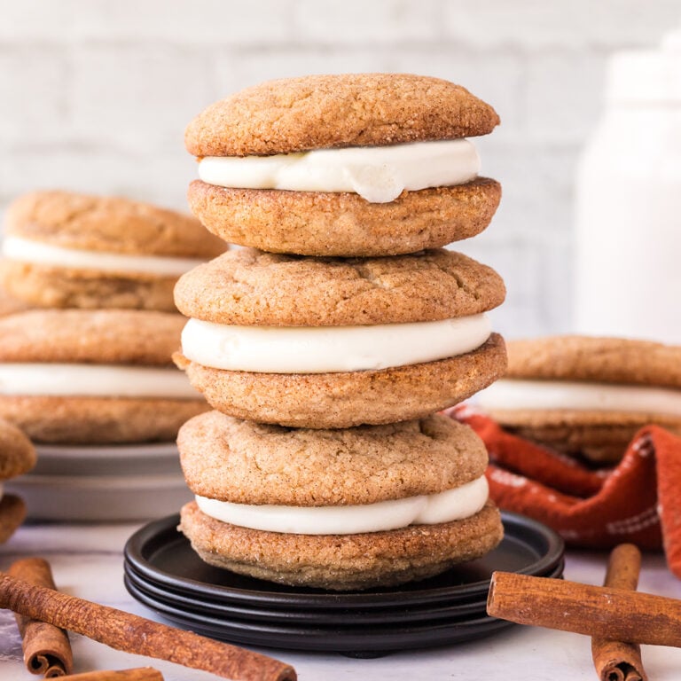 Three Snickerdoodle Sandwich Cookies stacked together on black plate.