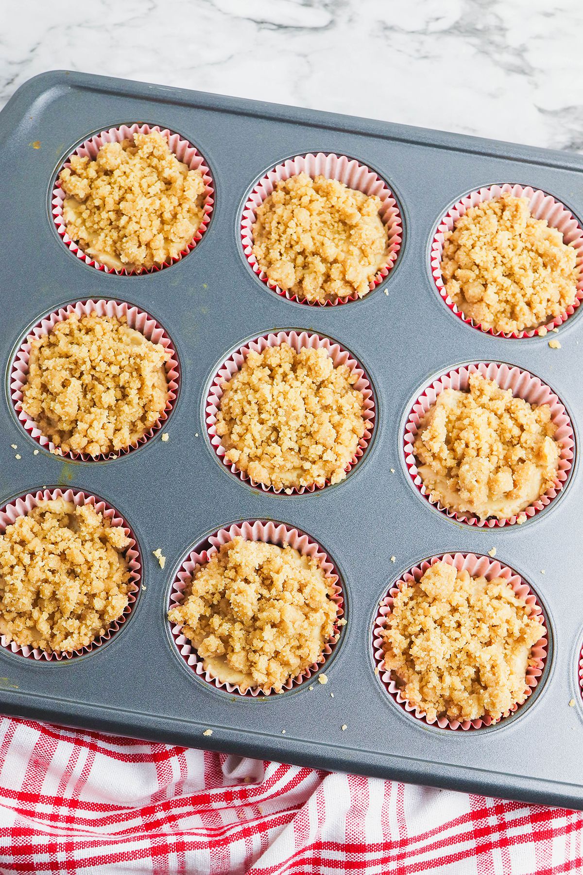 Crumble topping is added over the muffin batter in the muffin pan.
