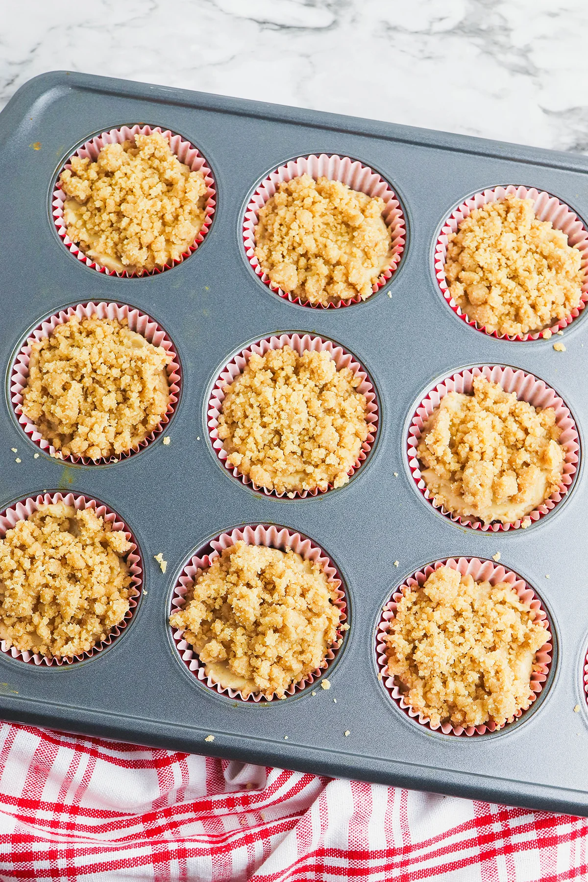 Crumble topping is added over the muffin batter in the muffin pan.