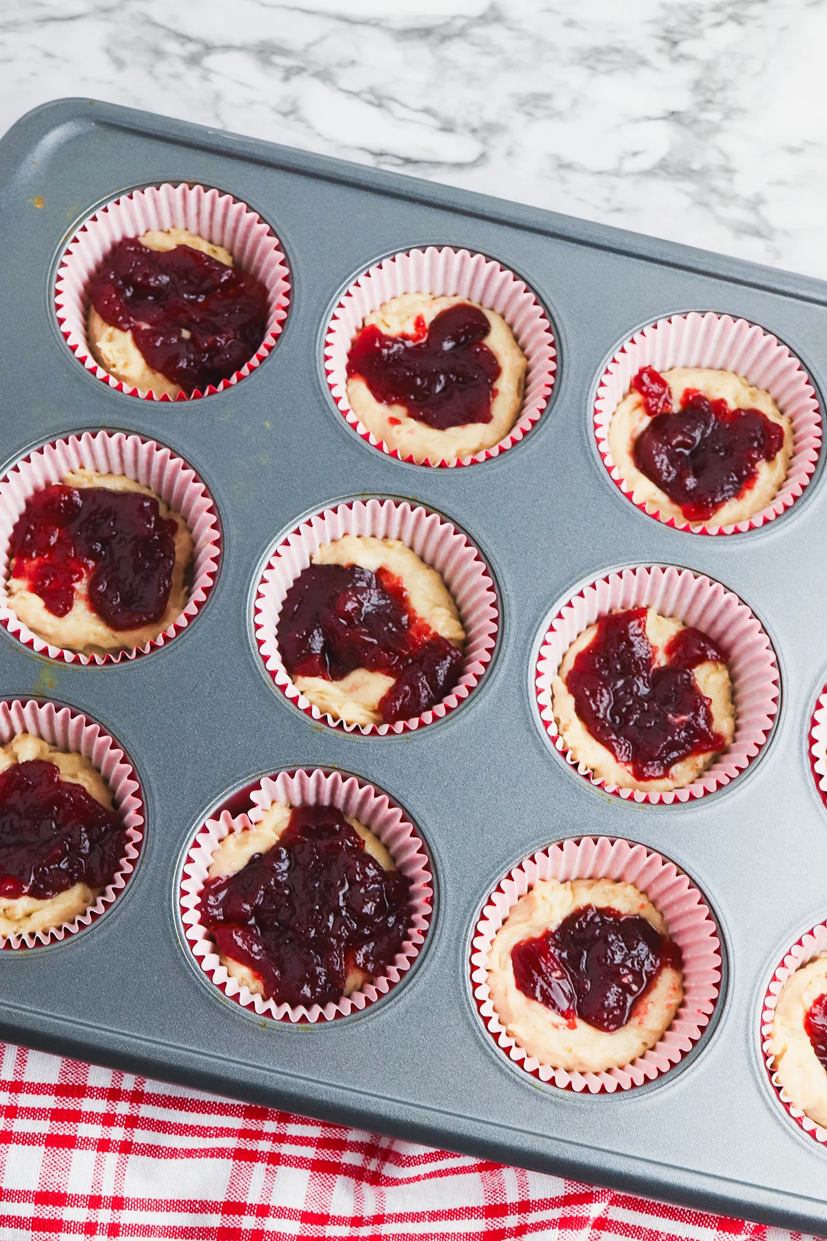 A layer of cranberry sauce is added over the muffin batter.