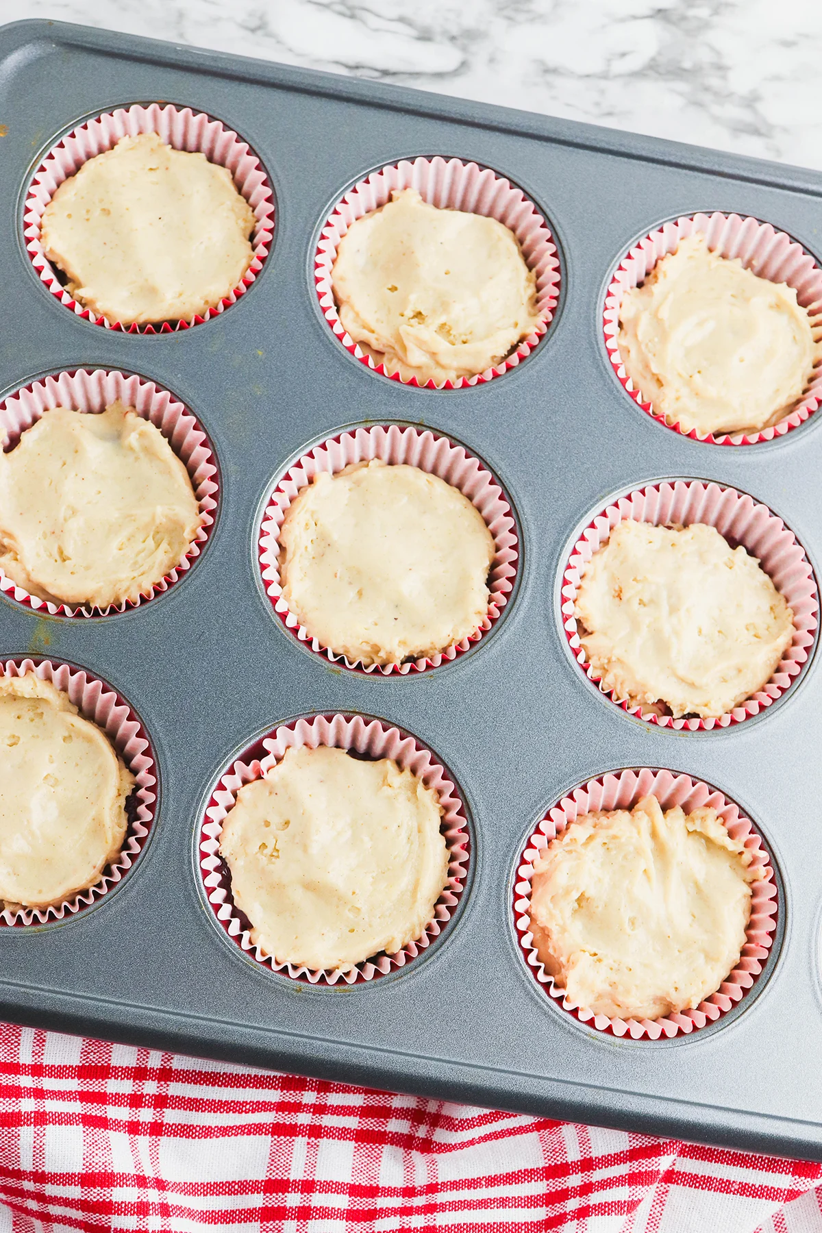 A layer of muffin batter is added over the cranberry sauce in the muffin pan.