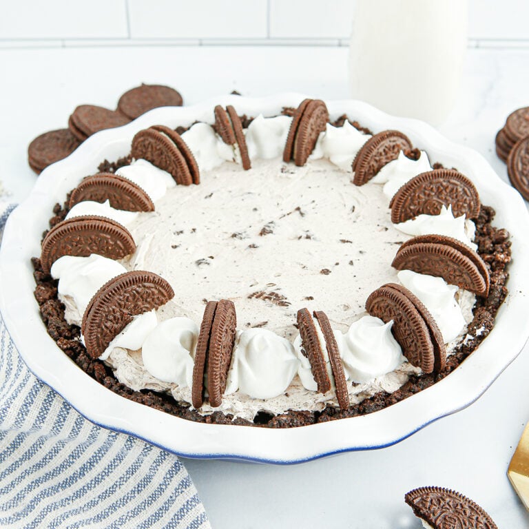 Oreo Cream Pie topped with whipped cream and Oreo cookies in white pie dish.