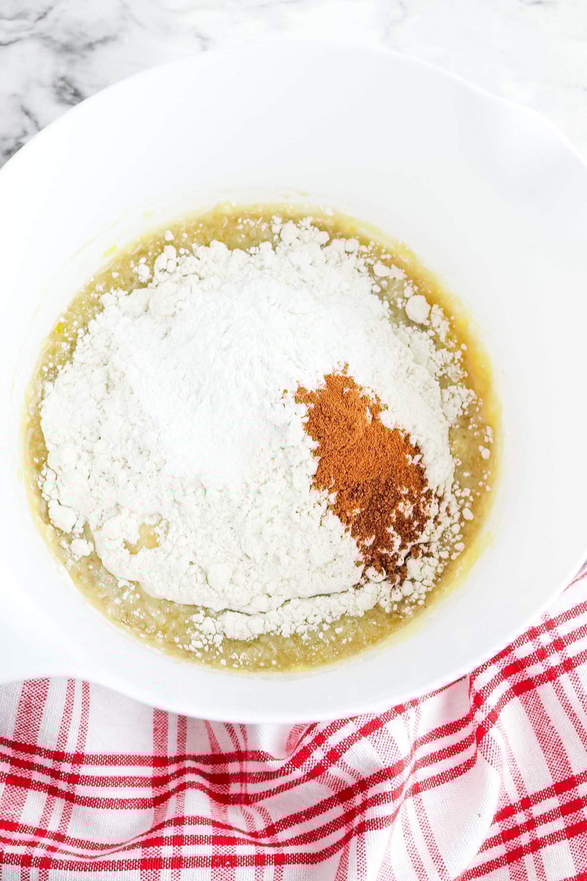 Flour, baking powder, cinnamon, nutmeg, and salt are added to the mixing bowl.
