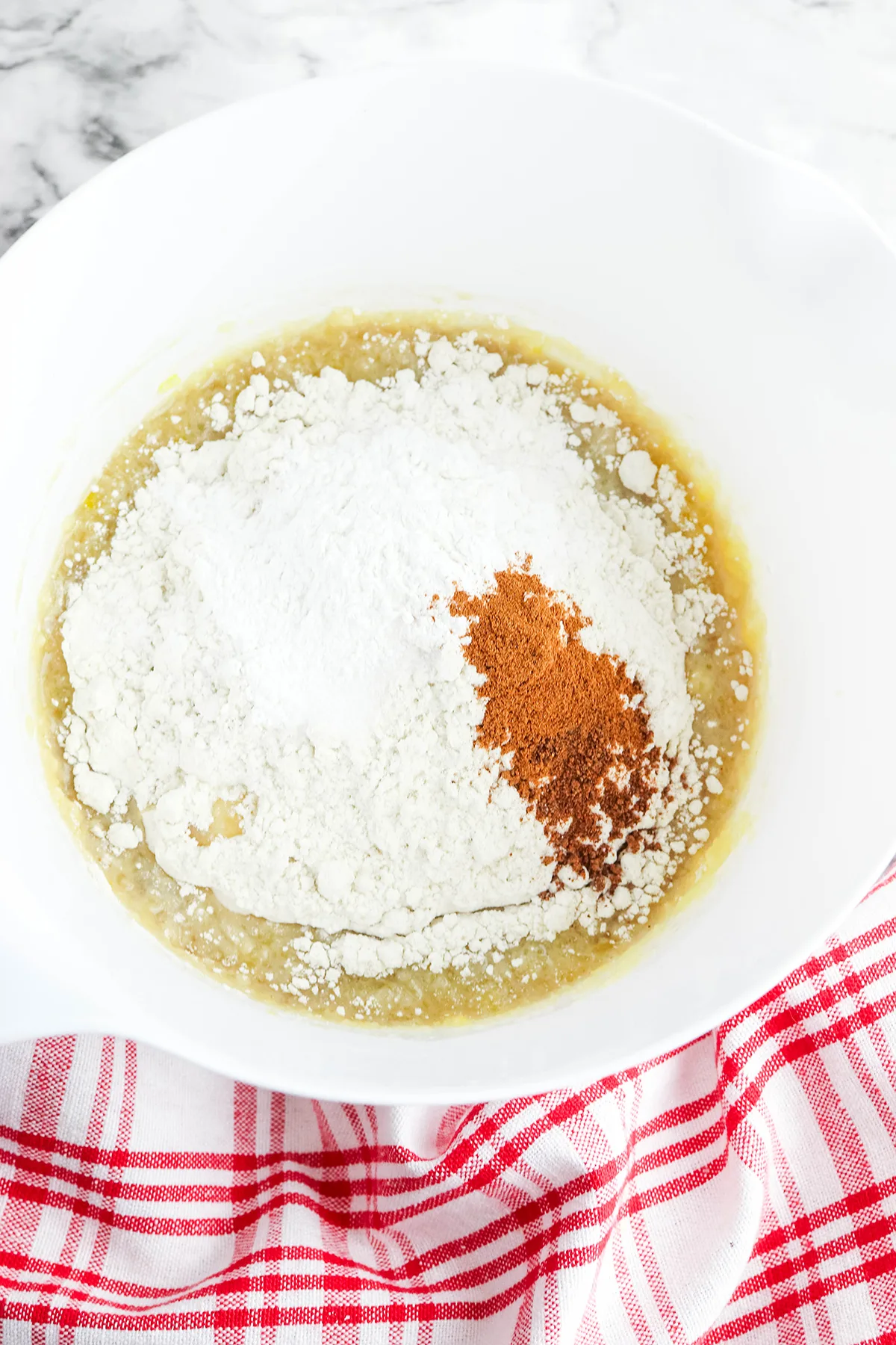 Flour, baking powder, cinnamon, nutmeg, and salt are added to the mixing bowl.