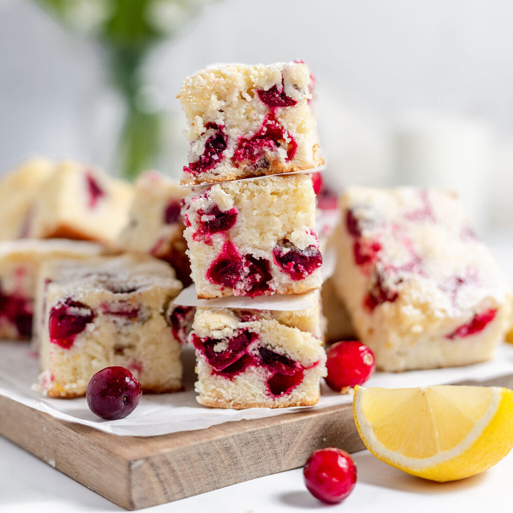 Cranberry Lemon Bars stacked on a wooden serving board.