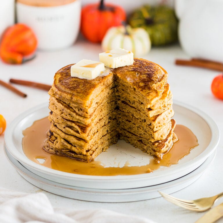 A stack of Pumpkin Pancakes on a plate topped with syrup.