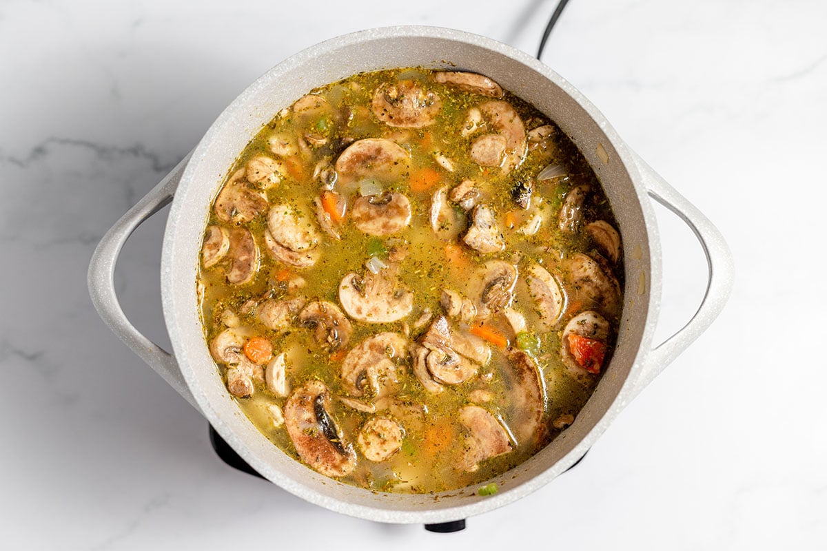 Chicken broth added to chicken and vegetables in large pot.