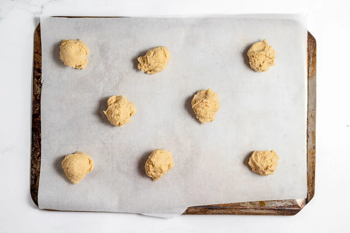 Cookie dough dropped by spoonful onto a cookie sheet.