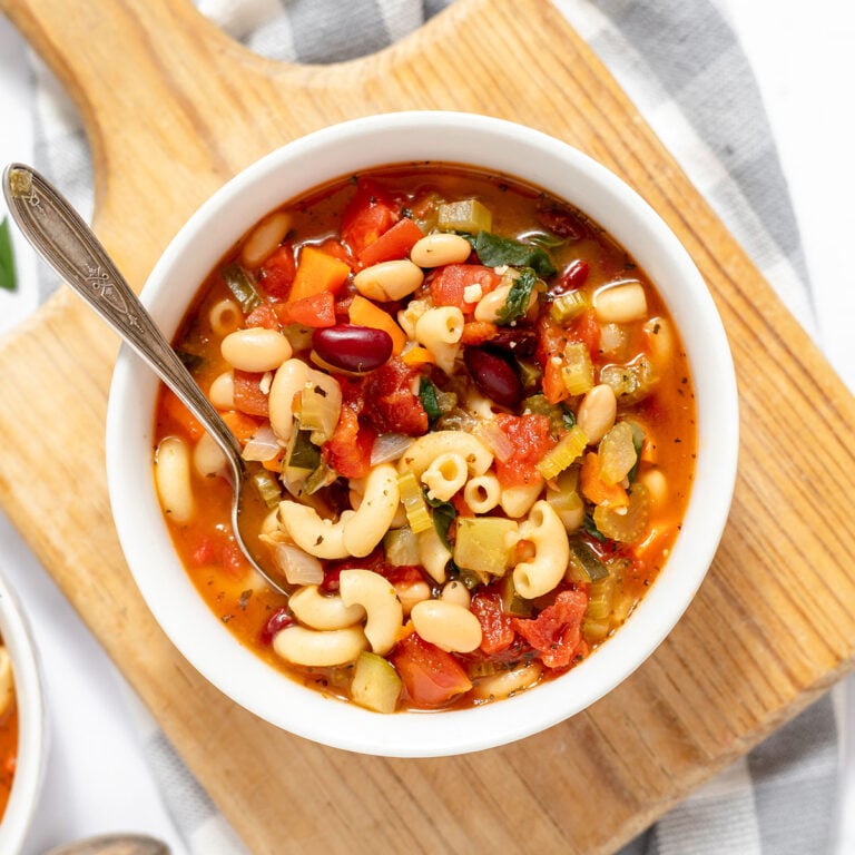 Serving of Minestrone Soup in a white bowl on a wooden serving board.