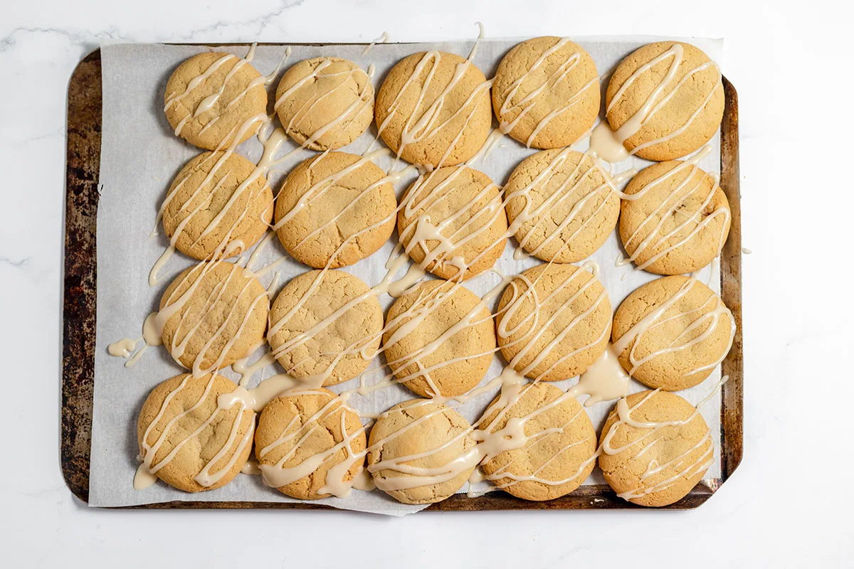 Maple Brown Sugar Cookies drizzled with maple icing on a baking sheet.