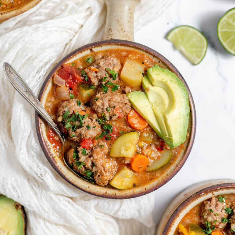 A serving of Mexican Meatball Soup in a bowl topped with avocado slices.