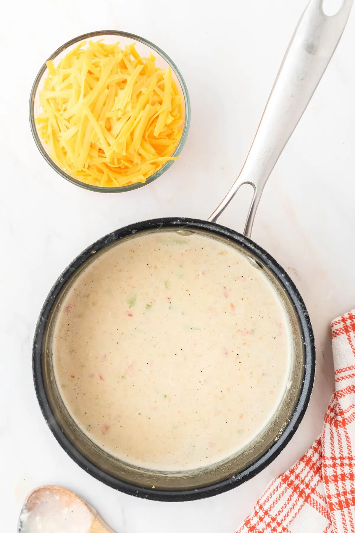 Shredded cheese is ready to add to the soup mixture in the saucepan.