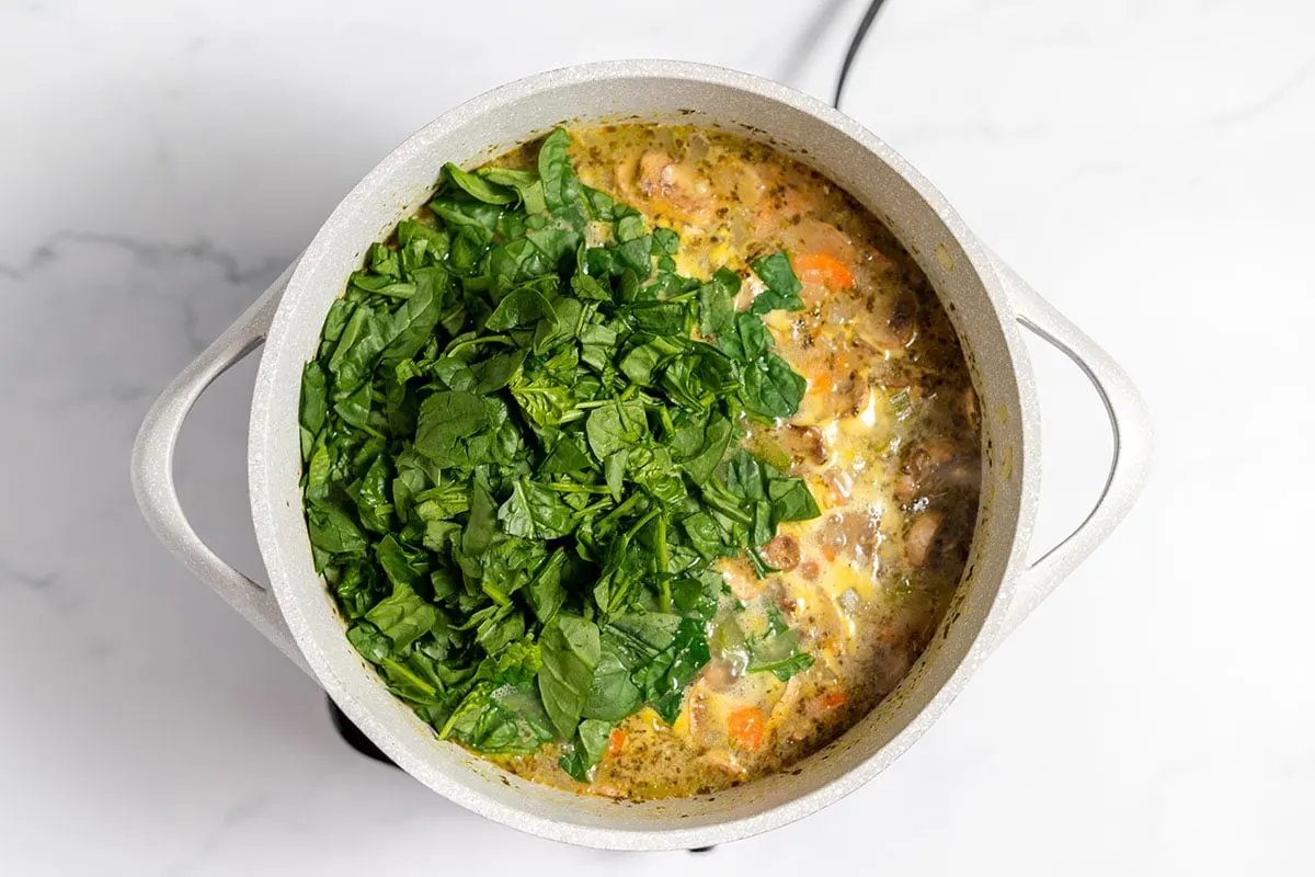Spinach added to chicken mushroom soup in large pot.