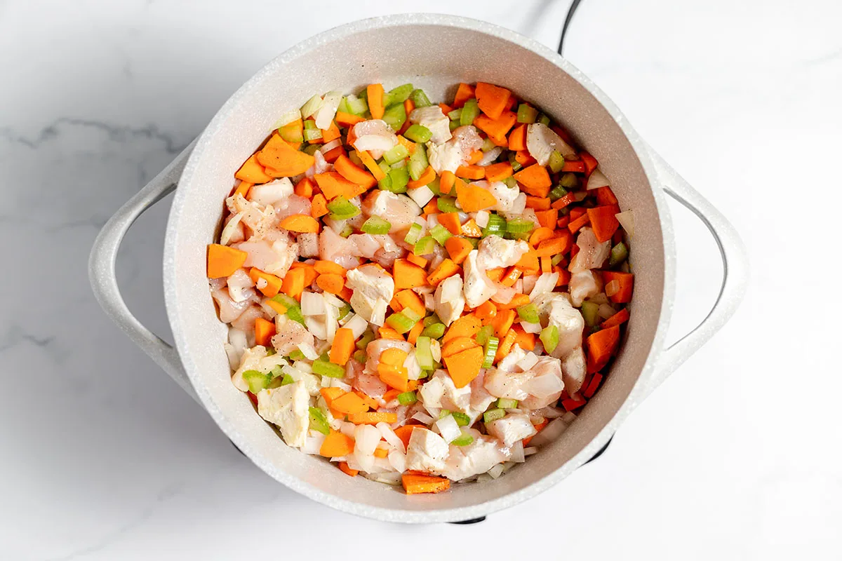 Chicken, onions, carrots, and celery sauteed in a large pot.