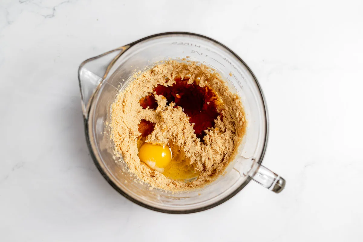 Egg, maple syrup, vanilla, and maple extract are added to the butter-sugar mixture in the mixing bow.