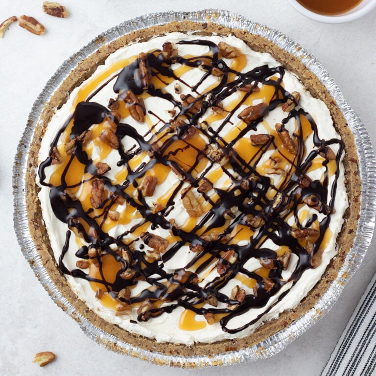 No-bake turtle cheesecake topped with chocolate syrup, caramel syrup, and chopped pecans.