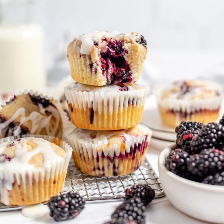 Blackberry muffins topped with icing on a wire rack.
