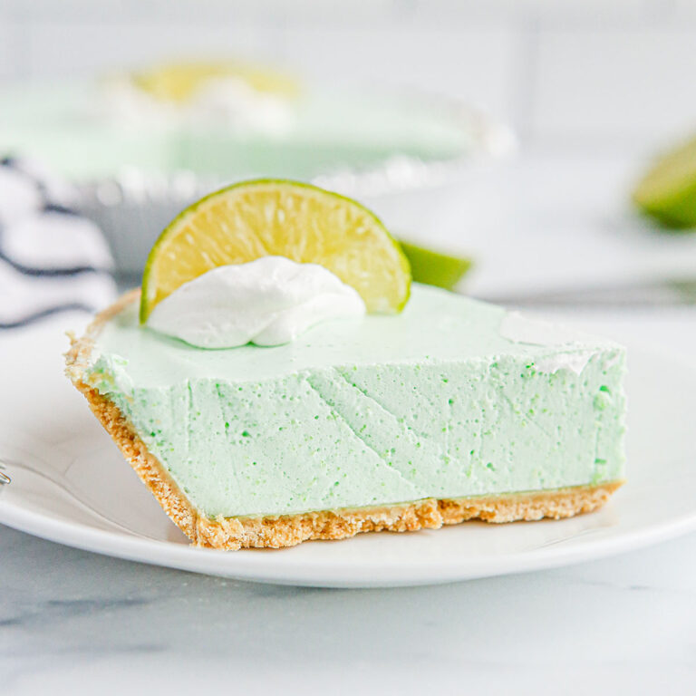 A slice of Lime Pie topped with whipped cream and a lime slice on a plate.