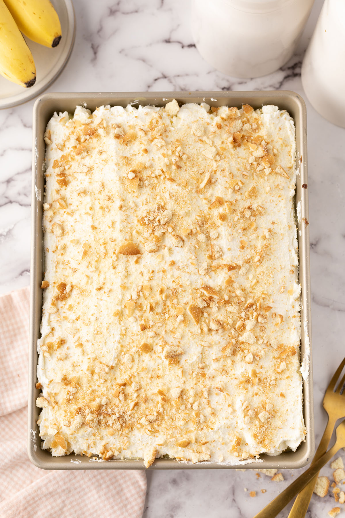 Homemade whipped cream frosting spread over top of cake with crumbled vanilla wafers in the baking pan.