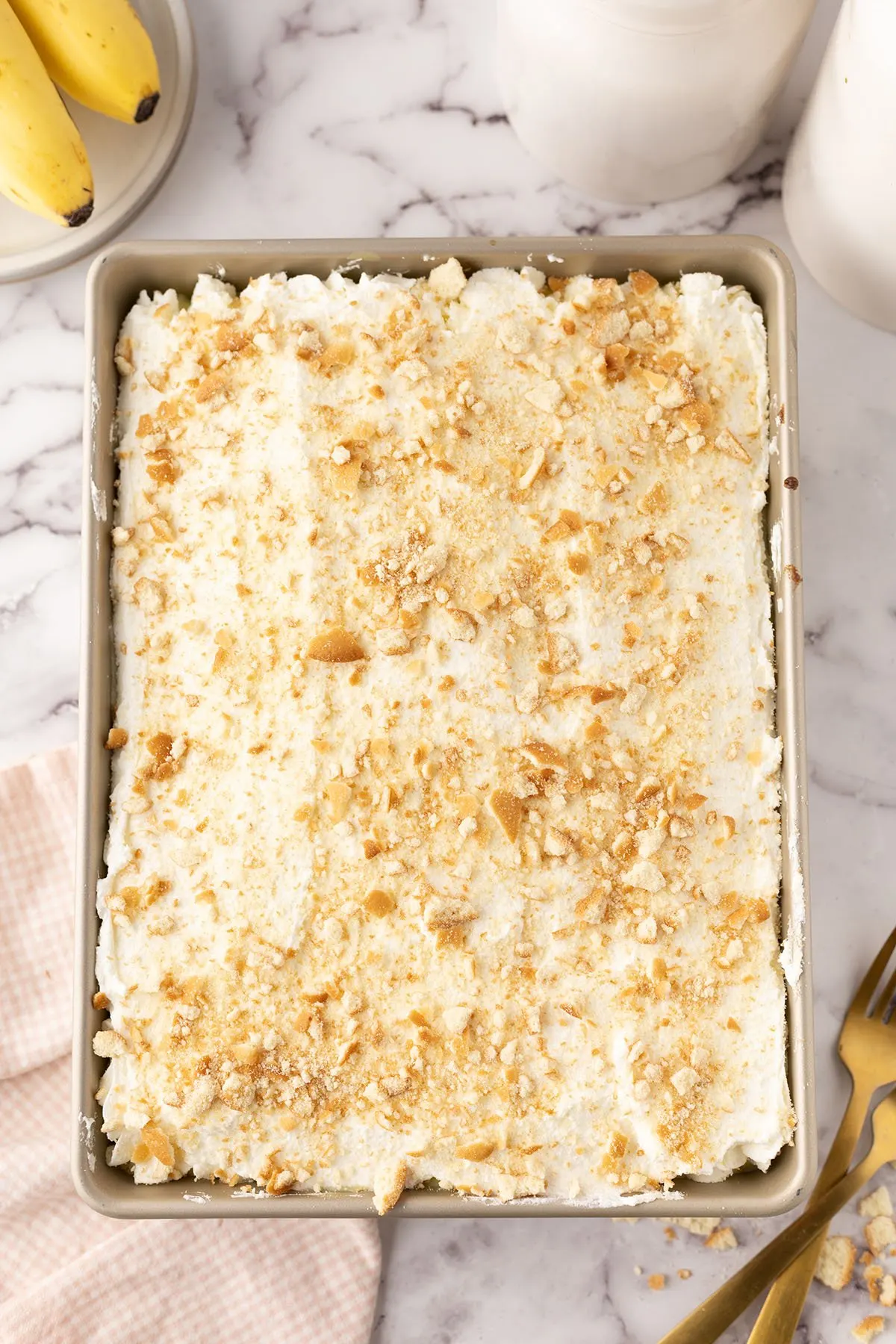 Homemade whipped cream frosting spread over top of cake with crumbled vanilla wafers in the baking pan.