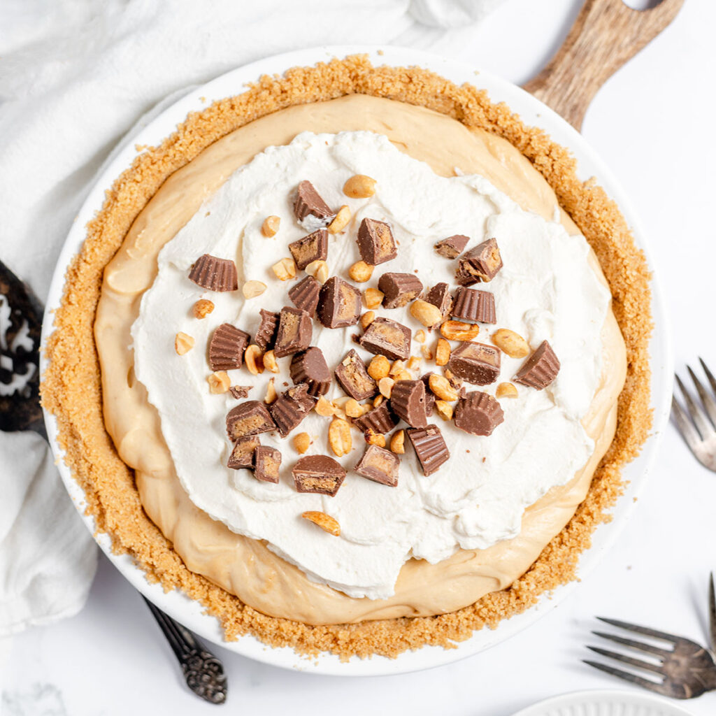 Peanut butter pie in pie plate topped with whipped cream and mini Reese's cups.