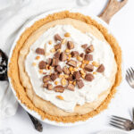 Peanut butter pie in pie plate topped with whipped cream and mini Reese's cups.