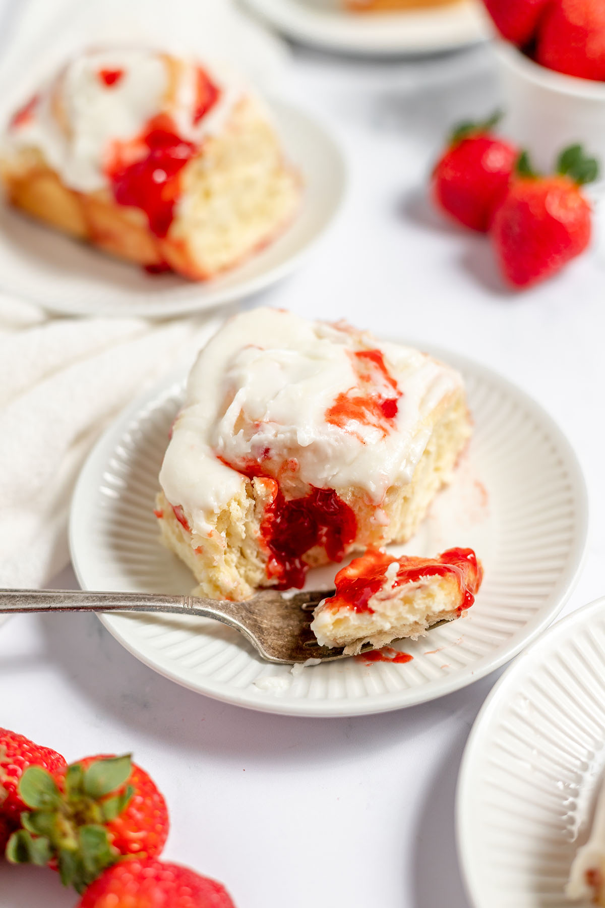 Strawberry cinnamon roll on a white plate with a bite on a fork.