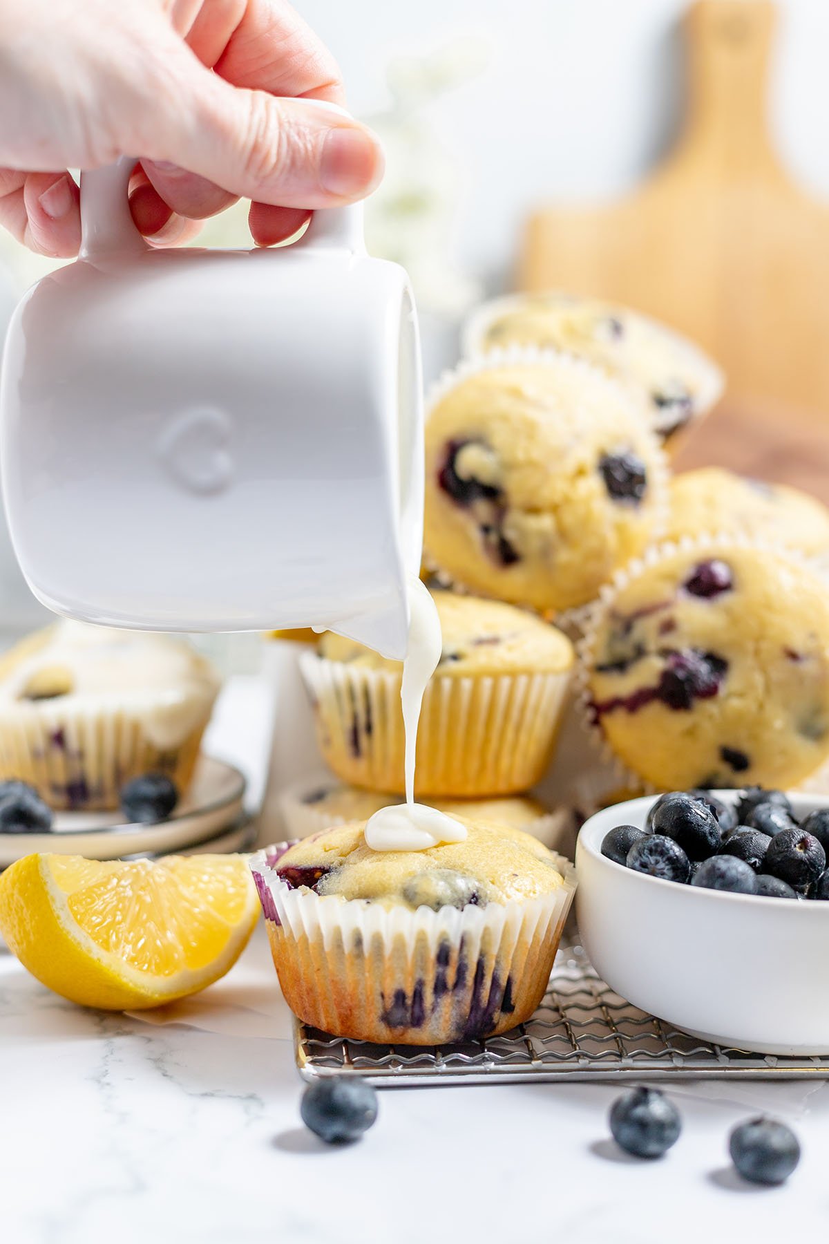 Lemon glaze is poured over a blueberry lemon muffin.