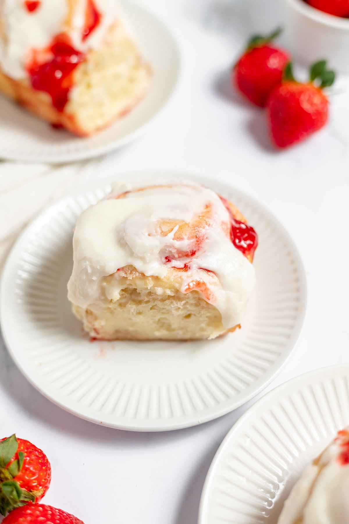 Strawberry Cinnamon Roll topped with icing on a plate.