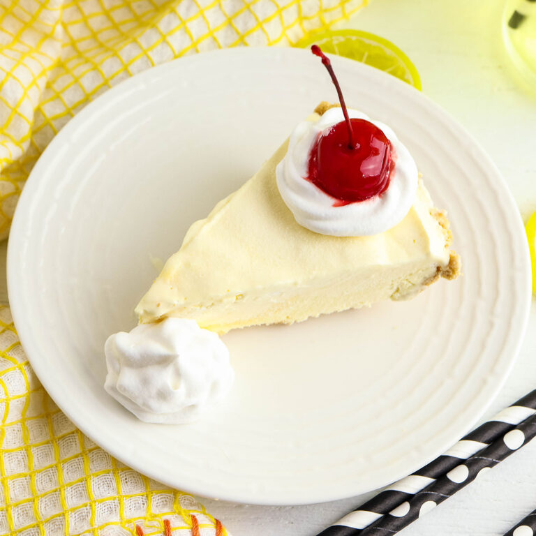 A slice of lemonade pie topped with whipped cream and a cherry on a plate.