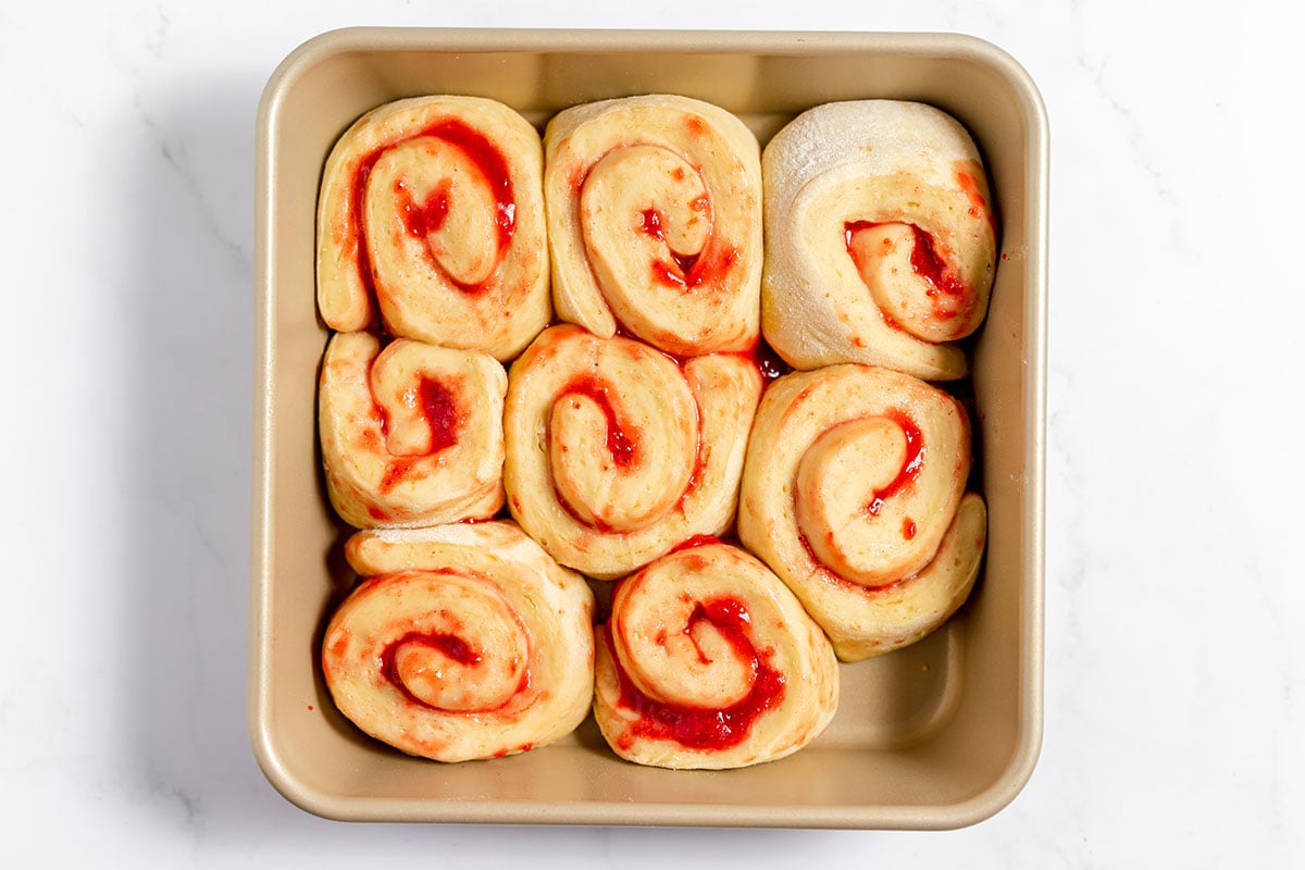 Strawberry Cinnamon Roll dough slices are risen in a baking pan and ready for oven.