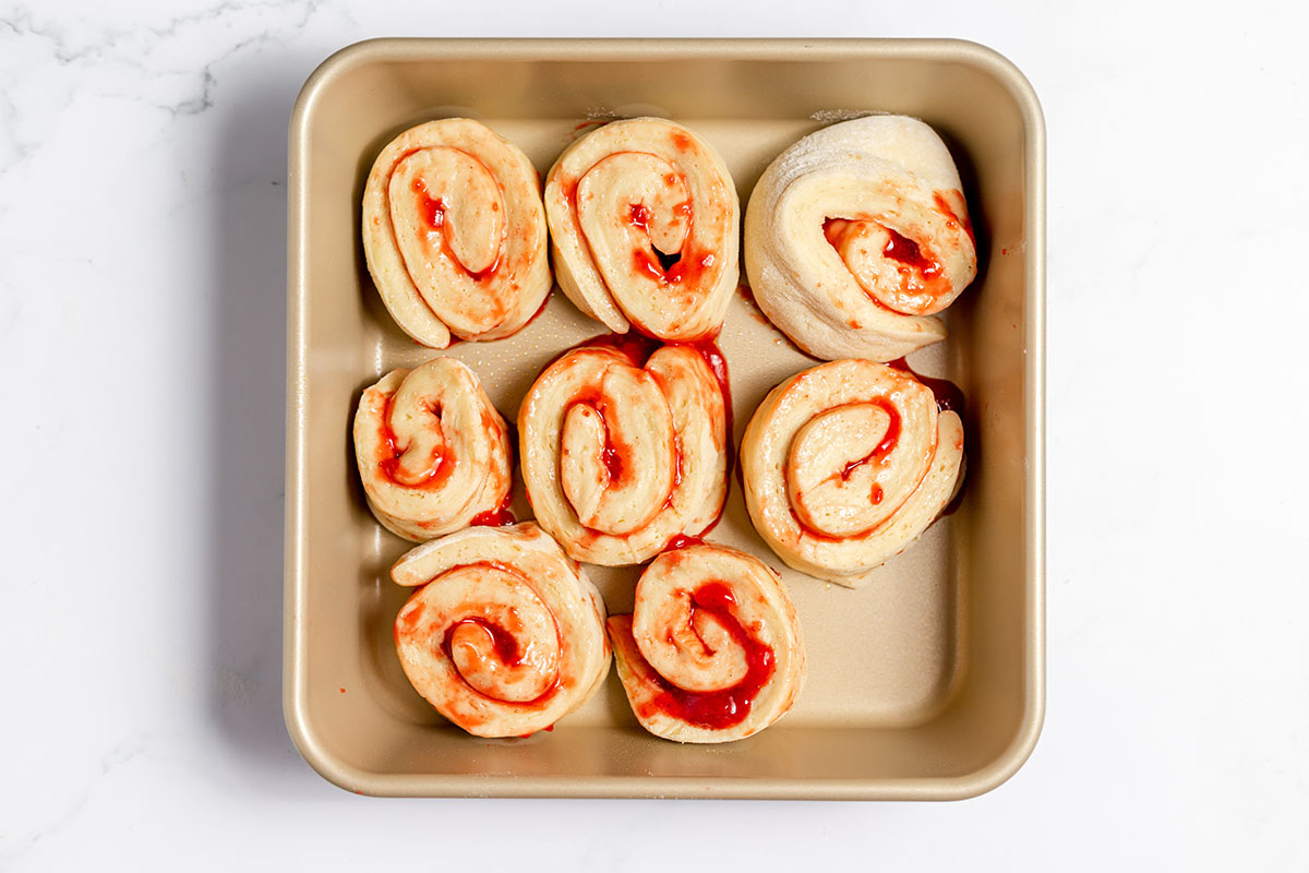 Strawberry Cinnamon Roll dough slices are placed in a baking pan to rise.