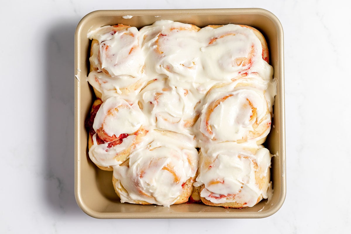 Strawberry Cinnamon Rolls topped with icing in a baking pan.