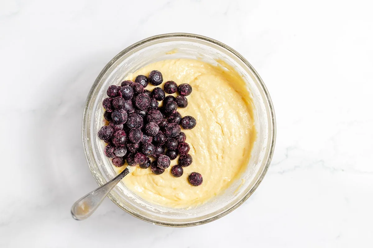 Blueberries added to the muffin batter in the mixing bowl.