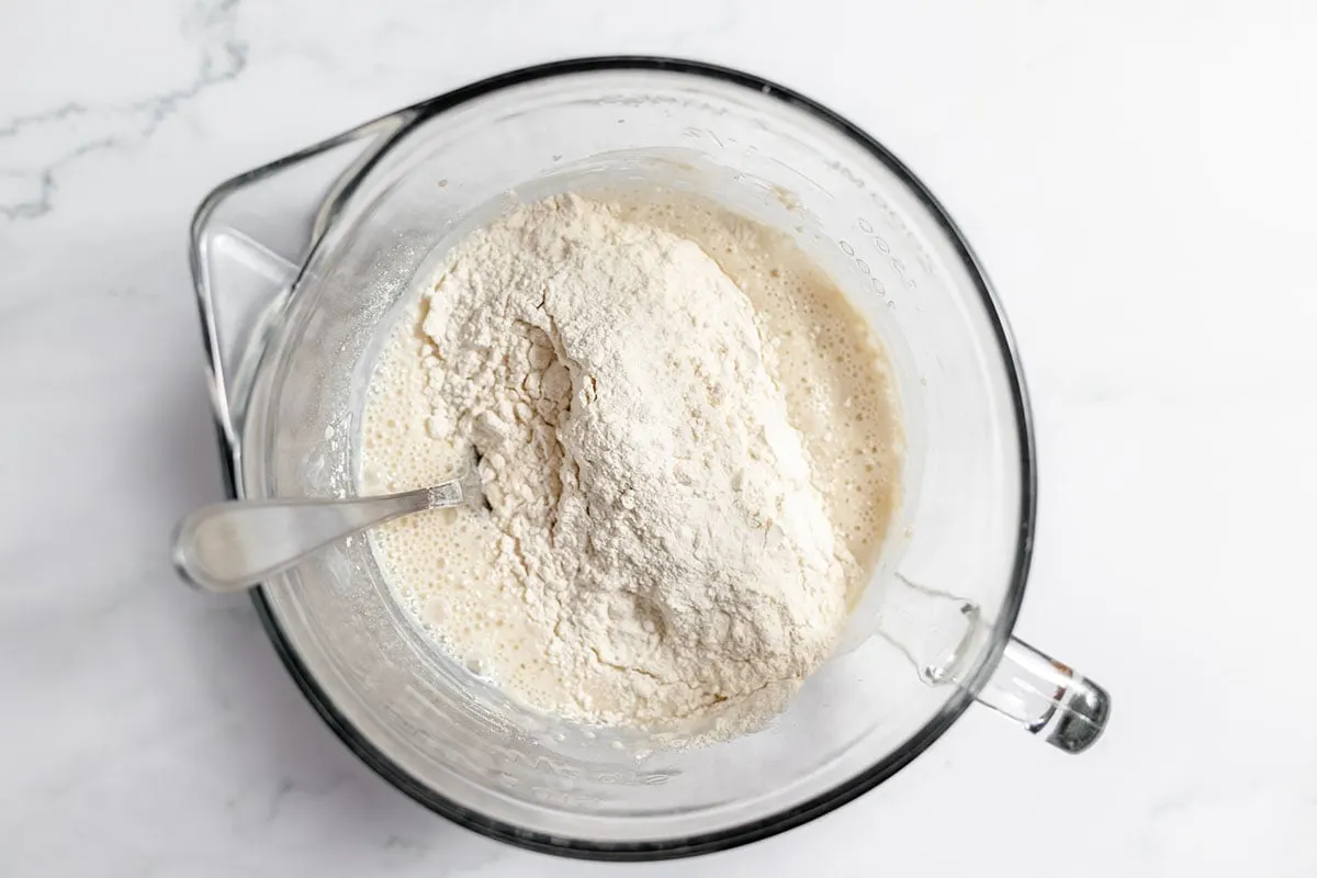 Flour, salt, and baking soda added to milk and yeast mixture in the mixing bowl.