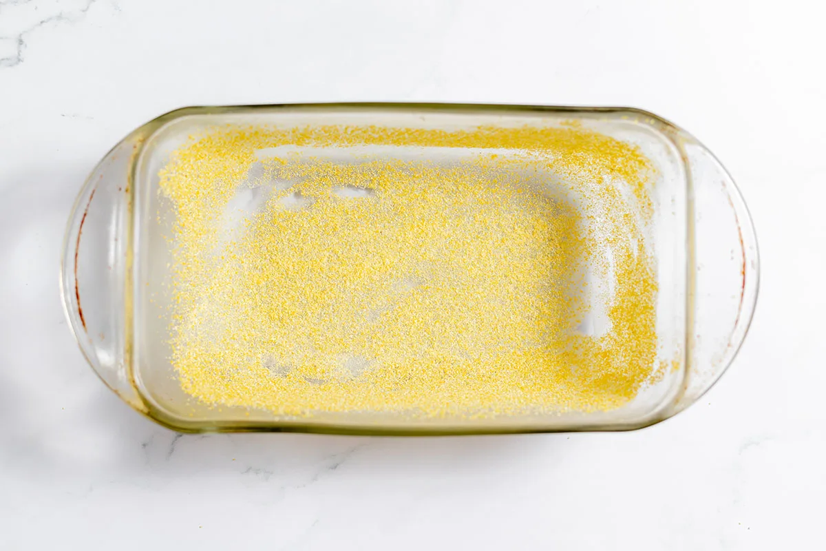 A glass loaf pan coated with butter and cornmeal.