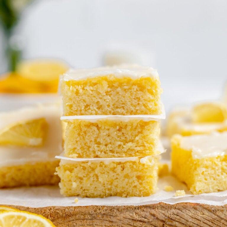 Three Lemon brownies are stacked on a wooden serving board.