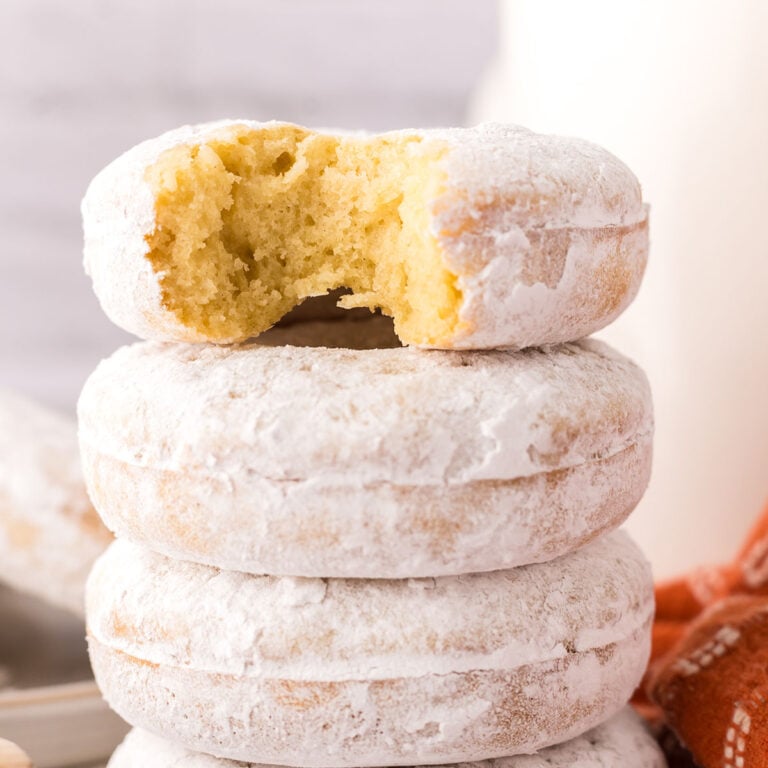 Powdered Donuts stacked together with a bite out of the top one.