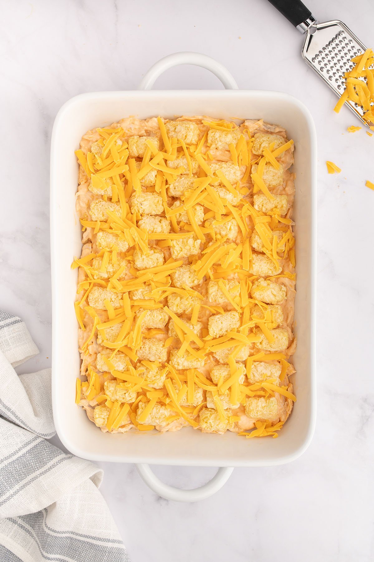 Cheese is added over the top of the tater tots and buffalo chicken filling in the baking dish.
