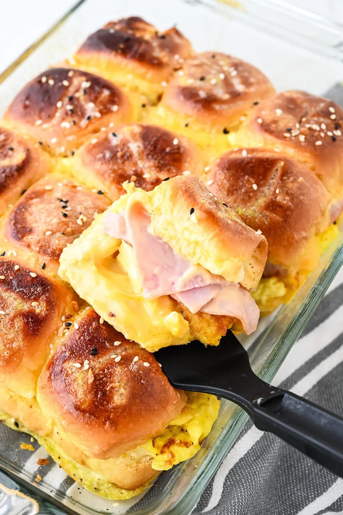 Baked Breakfast sliders in a glass baking dish with one roll on a serving spatula.