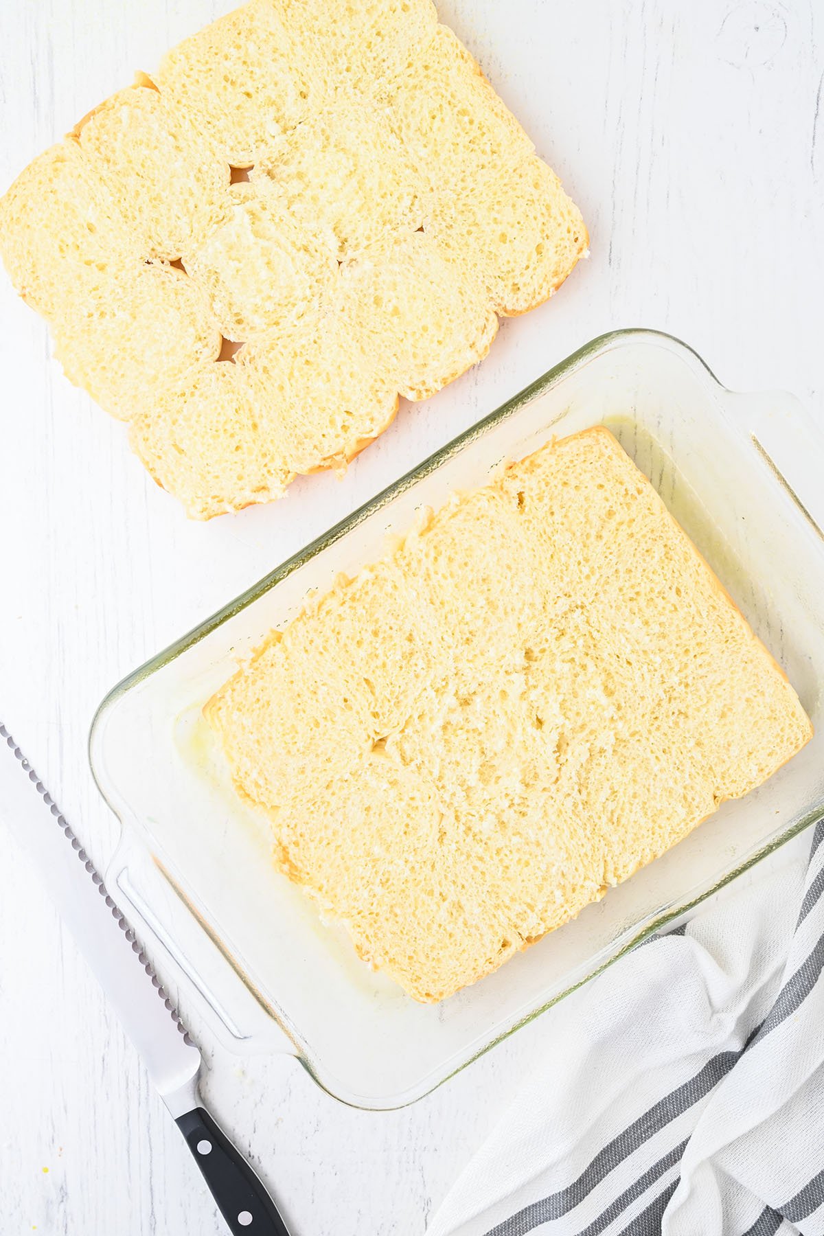 Hawaiian-style rolls are cut in half, and the bottom half placed in a glass baking dish.