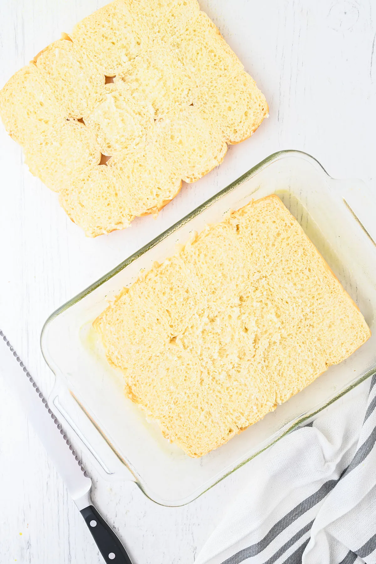 Hawaiian-style rolls are cut in half, and the bottom half placed in a glass baking dish.