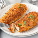 Two Italian Chicken Cutlets served on a white plate with a bite on a fork.