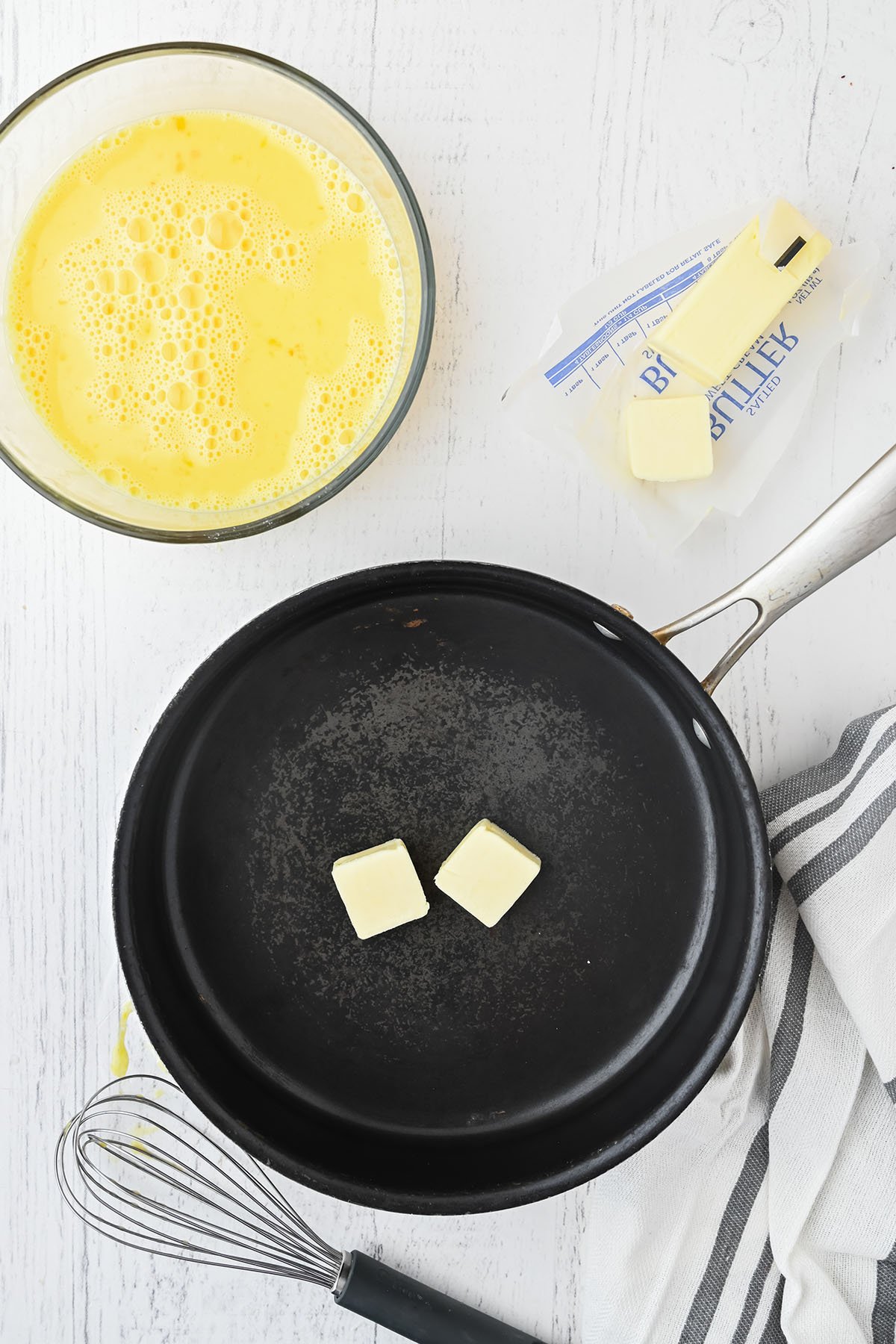 Skillet with butter to cook the eggs that are whisked in a bowl.