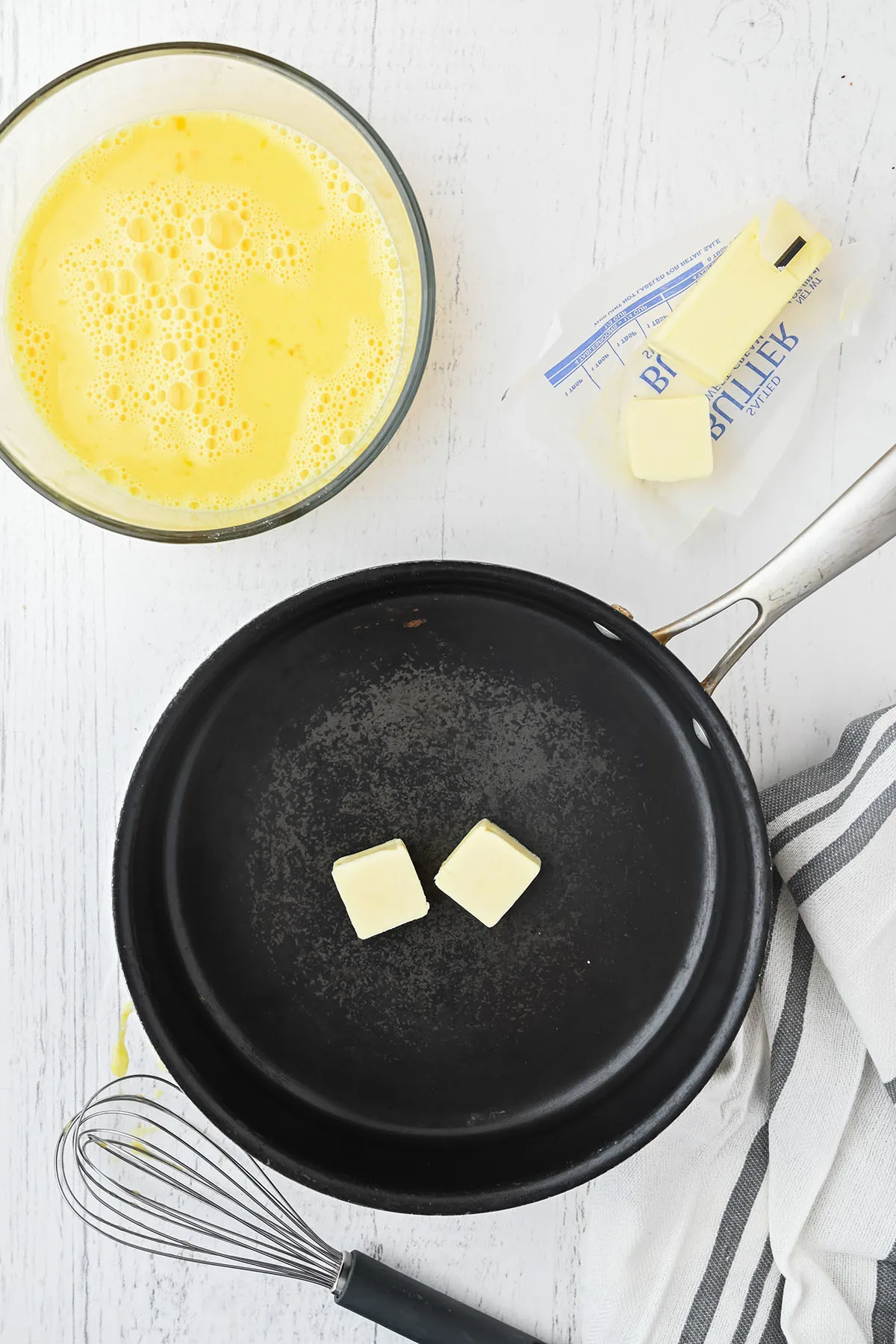 Skillet with butter to cook the eggs that are whisked in a bowl.
