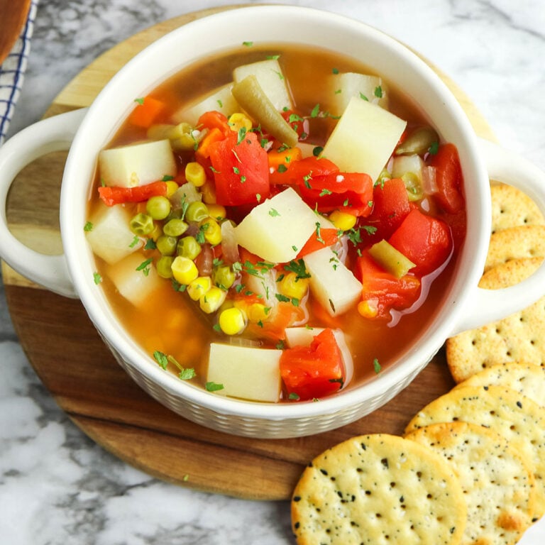 A bowl of Vegetable Soup on a wooden serving board with crackers.